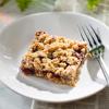 Raspberry almond breakfast bars stacked on a plate with visible oats and cranberries