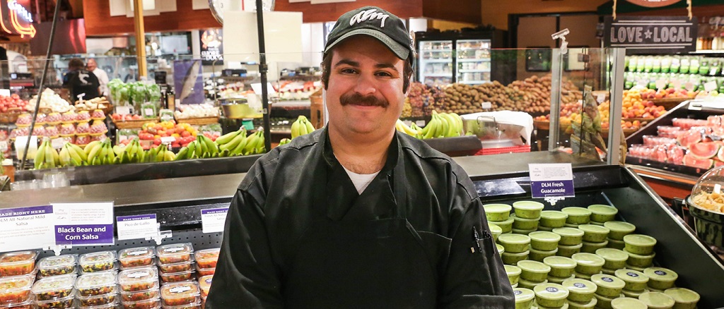 austin hieb standing in produce in front of the freshly made dlm salsa and gucamole