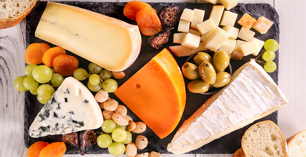 cheese board with bread, olives, apricots, almonds, and grapes