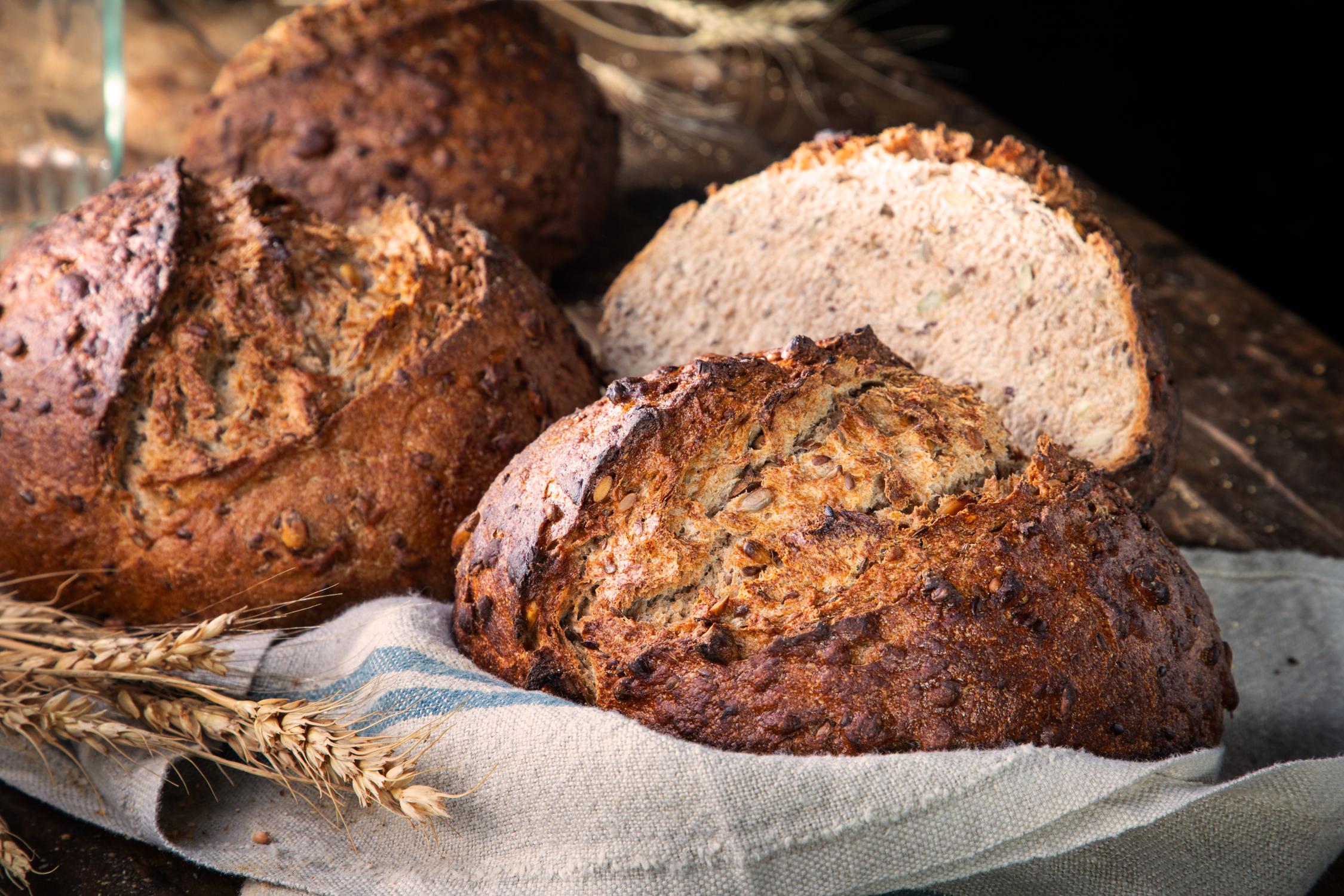 Dorothy Lane Market 100% Spelt Bread with Seeds — hearth-baked whole grain loaf with pumpkin and sunflower seeds on a wooden cutting board